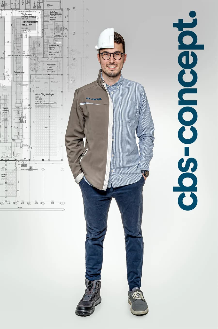 Sebastian Adam von cbs-concept, halb in Arbeitsjacke mit Schutzhelm, halb im Hemd, vor dem Layoutplan einer Backwarenproduktion